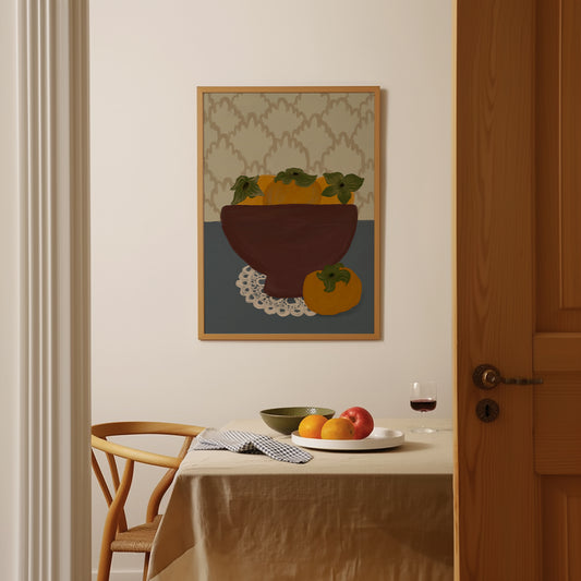 Persimmon still life art print in wooden frame, styled as kitchen wall art above a dining table with fruit and wine.