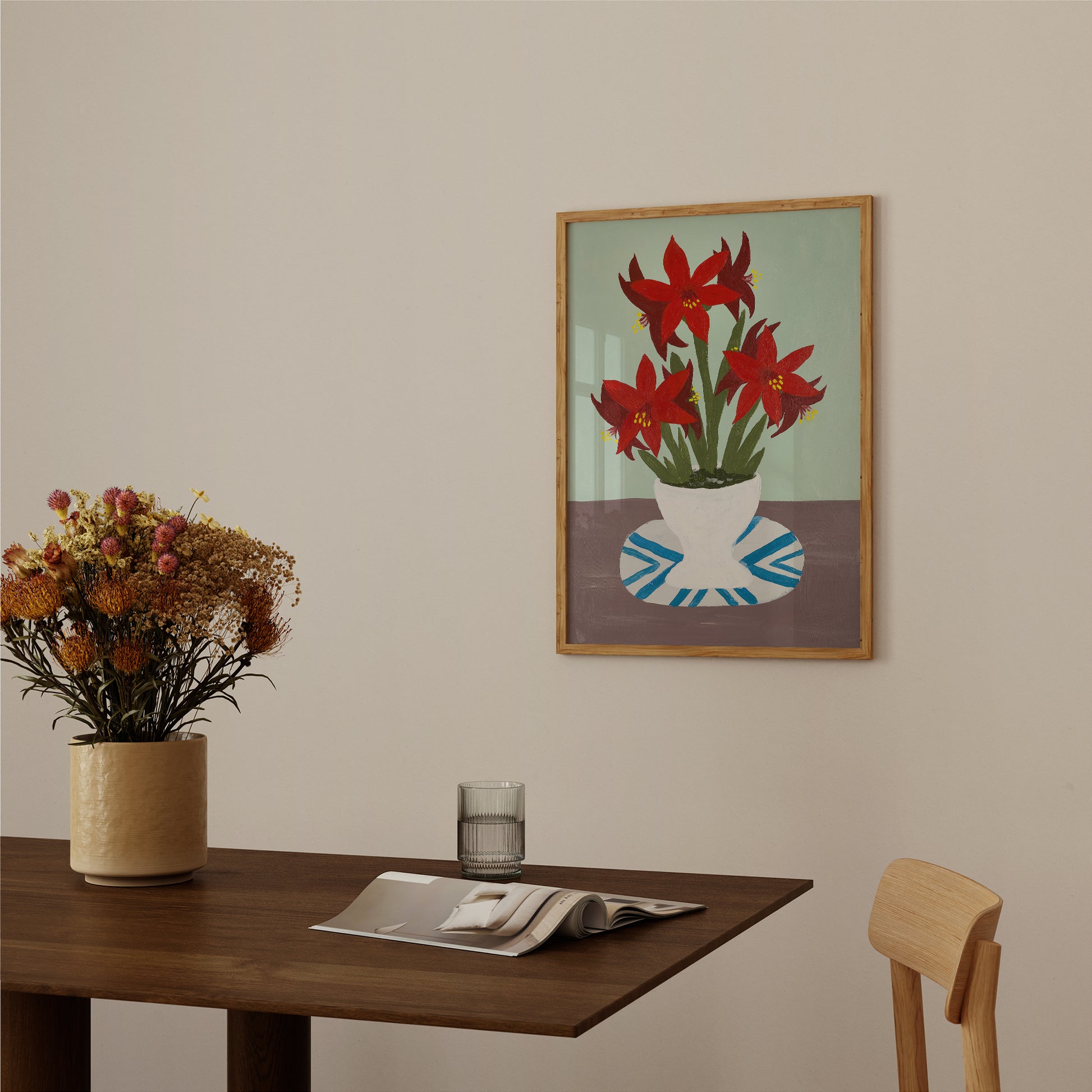 Framed red amaryllis wall art displayed above a wooden table with a neutral vase. Modern floral print for kitchen or dining room decor.