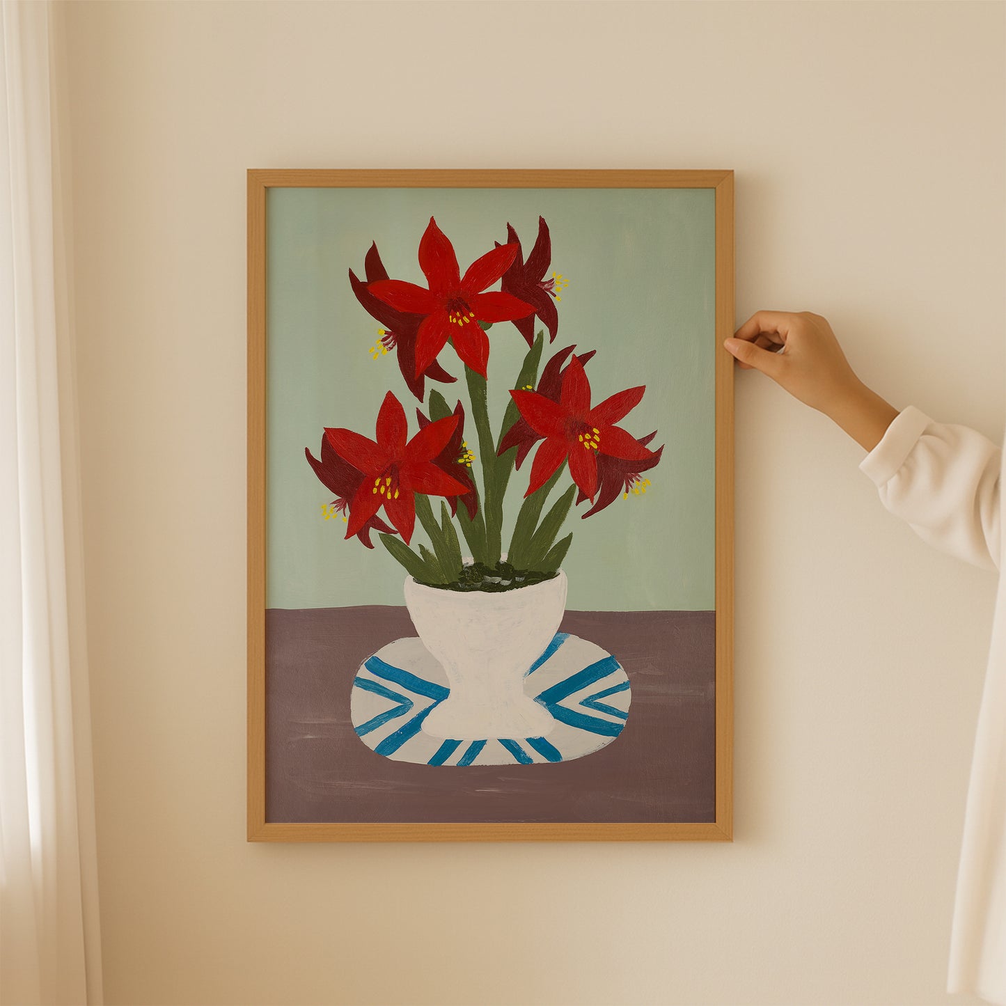 Person hanging framed red amaryllis still-life print. Floral wall art with bold red flowers and minimalist design for modern interiors.
