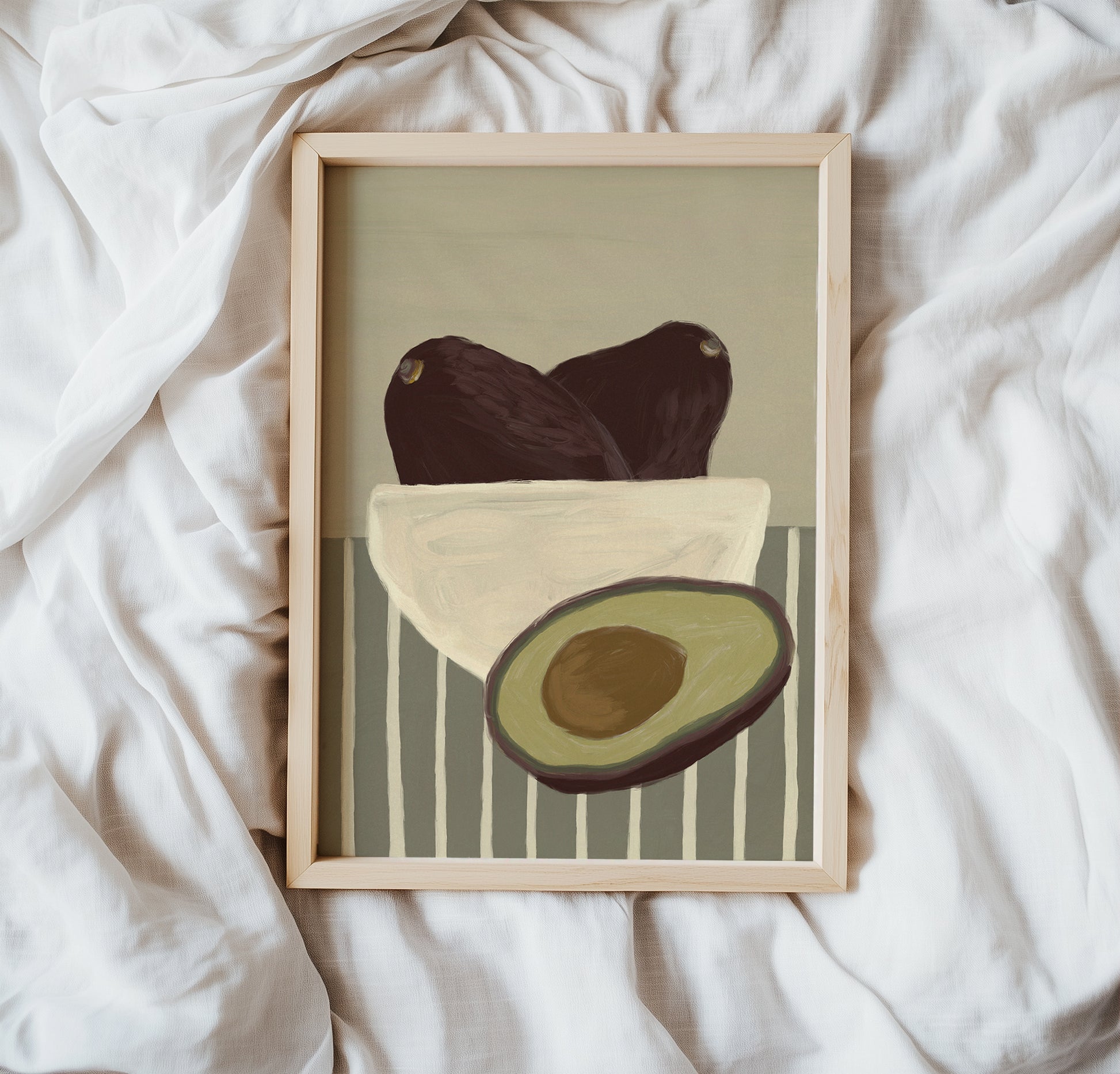 Framed avocado art print placed on white fabric, minimalist still life wall art poster with modern food illustration.