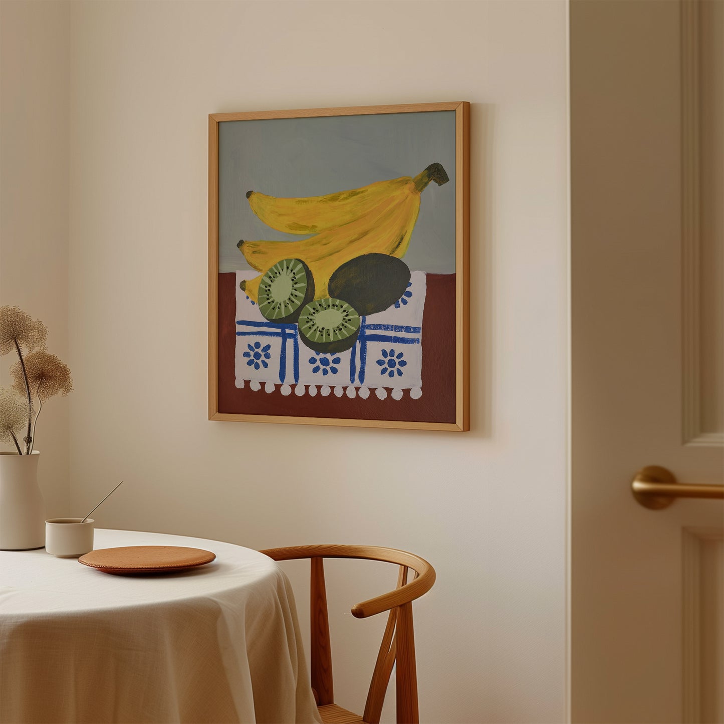 Framed acrylic painting art print of bananas and kiwis hanging in a minimalist dining room – colorful still life wall art for kitchen or breakfast nook decor.