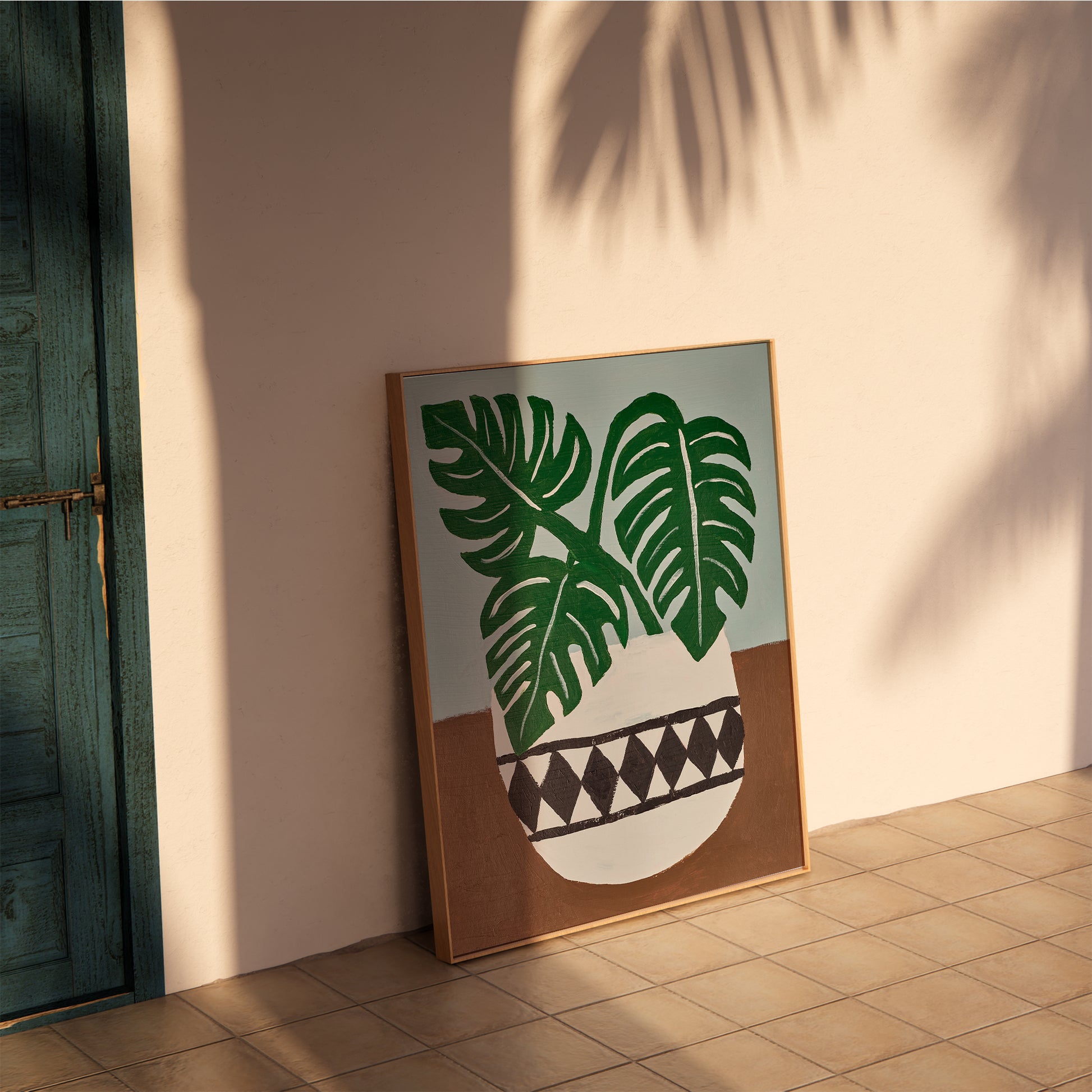 Framed monstera acrylic painting art print leaning on a sunlit terracotta wall – tropical botanical poster for boho, coastal, and mid-century interior decor.