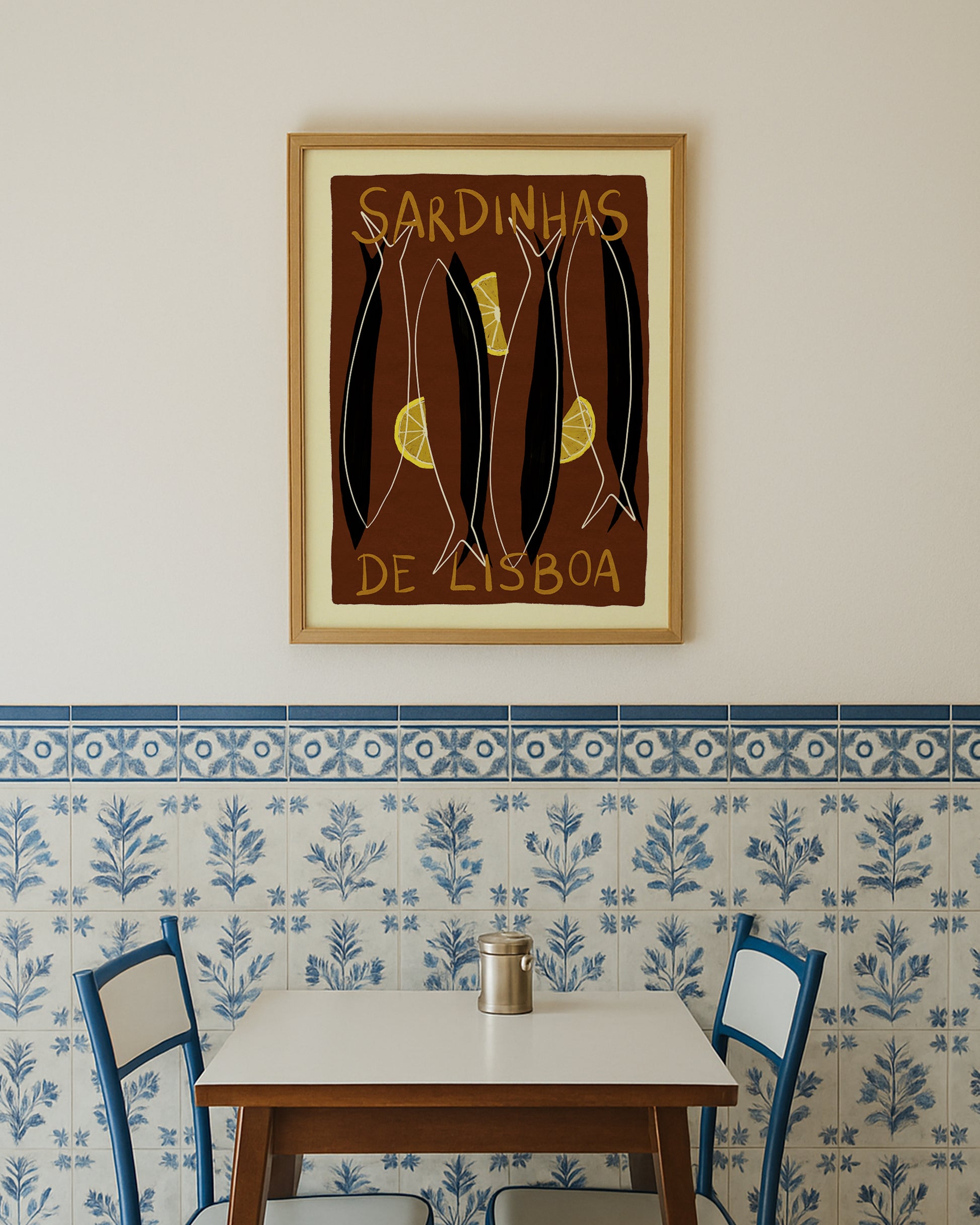 Framed sardines artwork on a wall with a table and chairs below a decorative tile pattern.