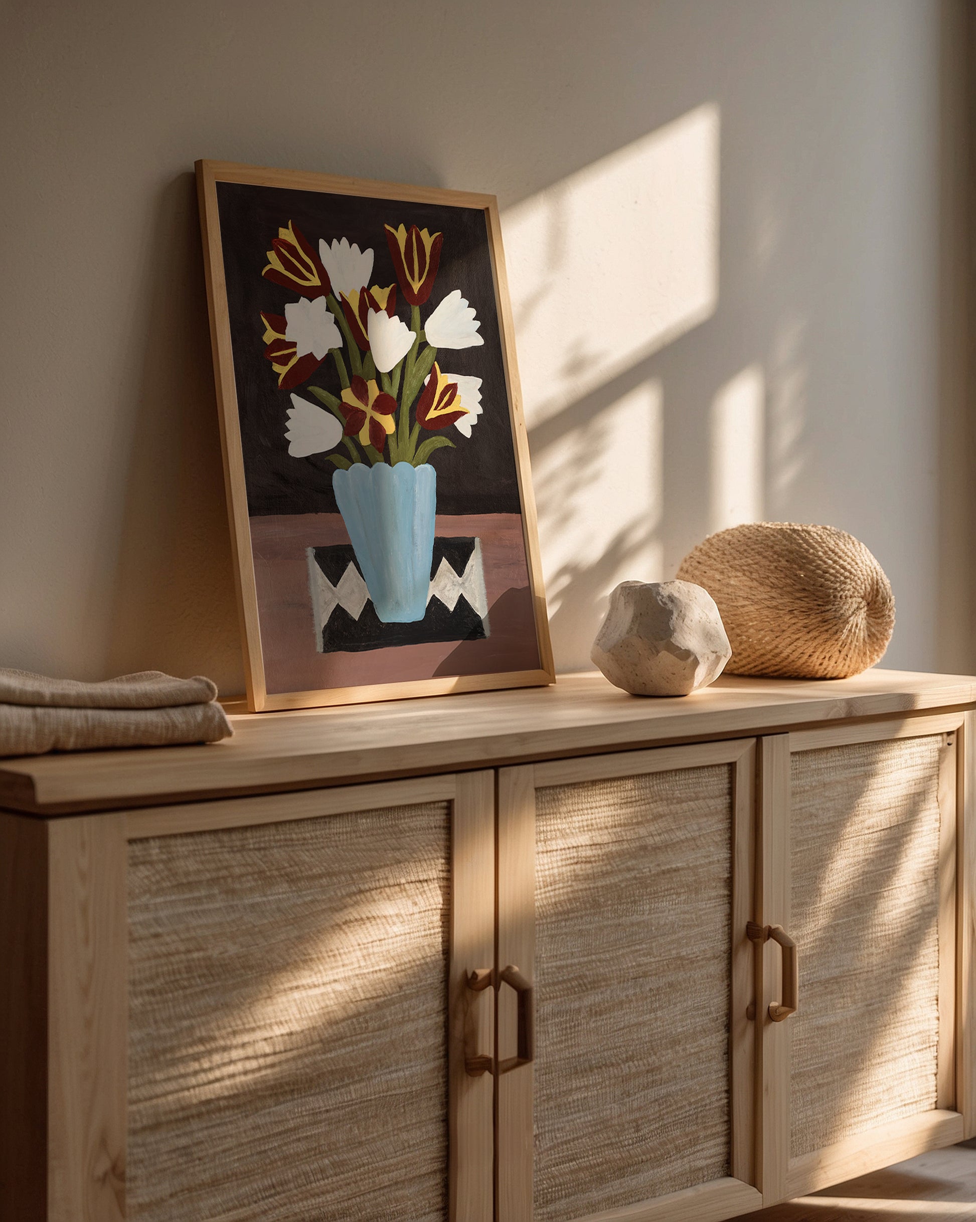 Tulip still life art print in a natural wood frame styled on a sideboard. Modern floral wall decor in earthy tones, perfect for boho or Scandinavian interiors.