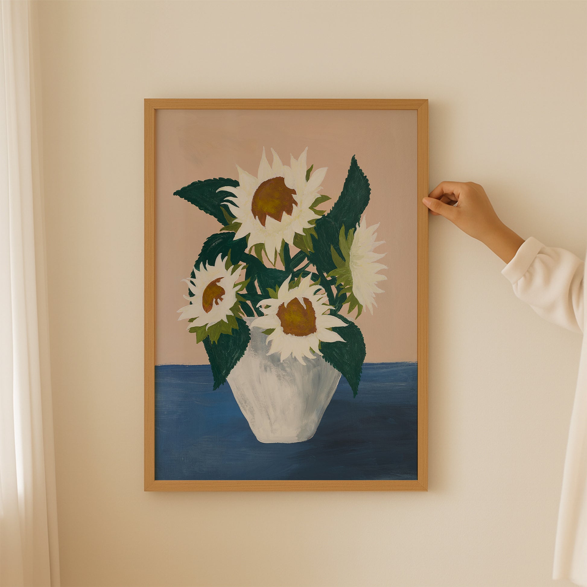 Person hanging framed sunflower still-life art print. Modern botanical wall decor with white flowers and blue-beige palette, mid-century inspired.